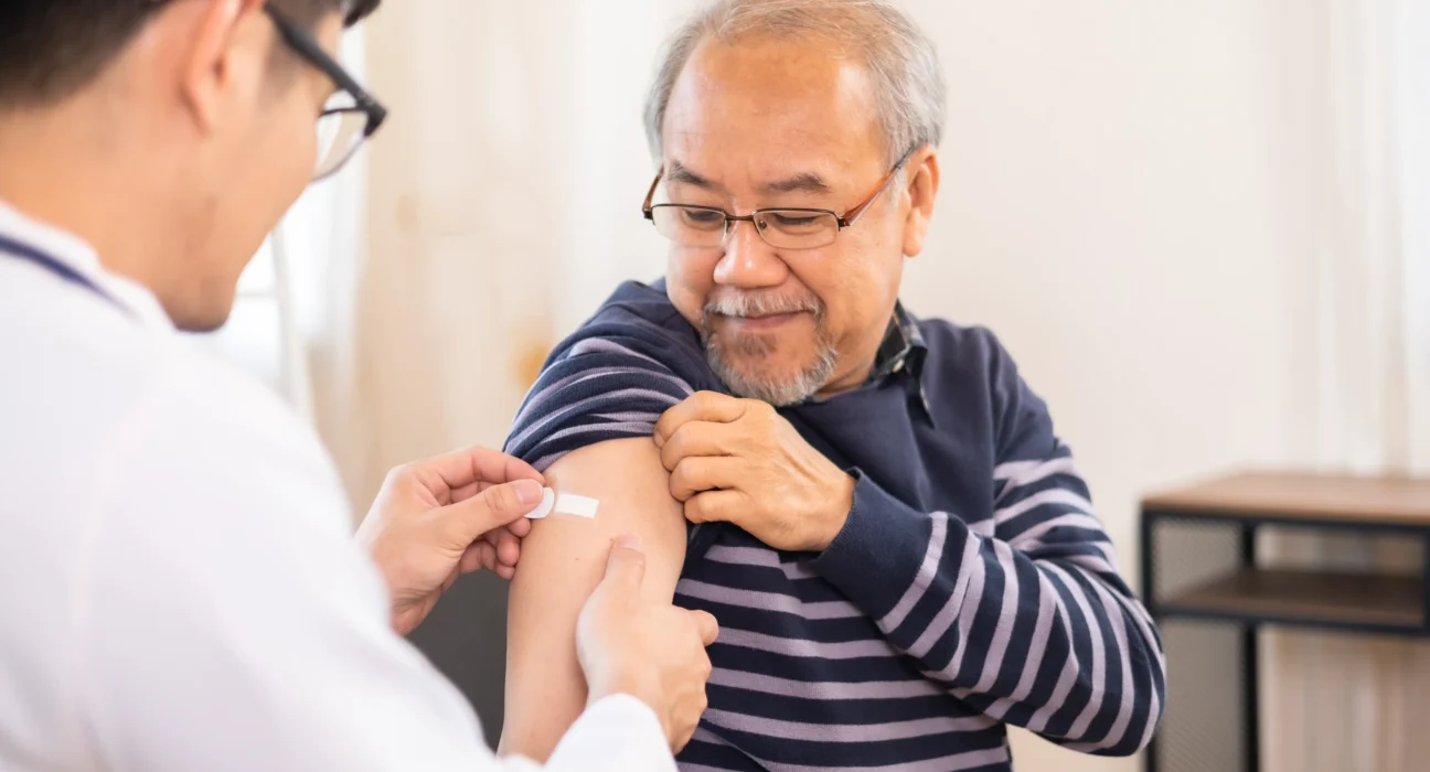 A smiling elderly man receives a shingles vaccine shot from a healthcare professional, symbolising the importance of immunisation against shingles and its complications.